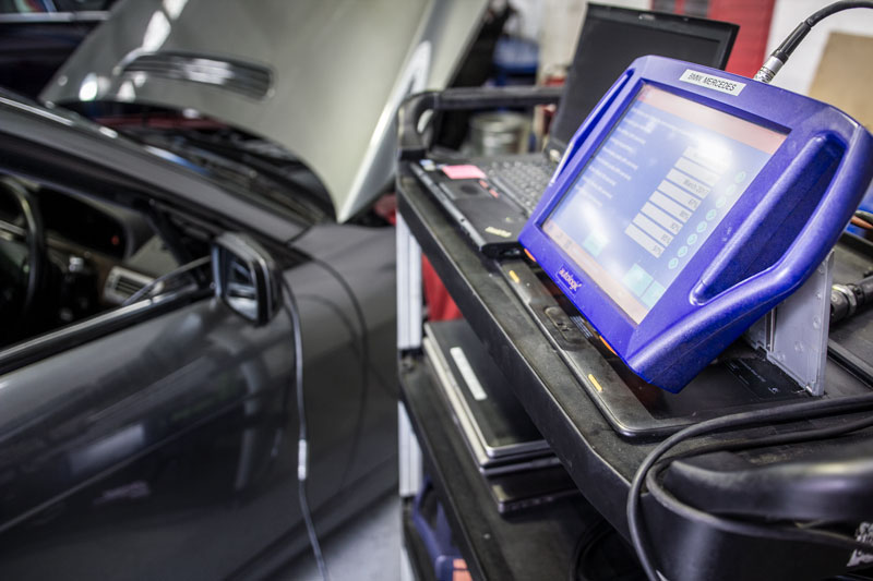 diagnostic tool sitting on tool shelf next to vehicle being diagnosed